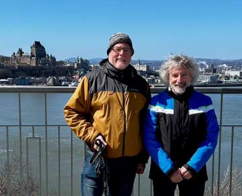 Two middle aged white men in warm jackets, clerks of montreal Monthly Meeting, smile to the camera in front of a river.