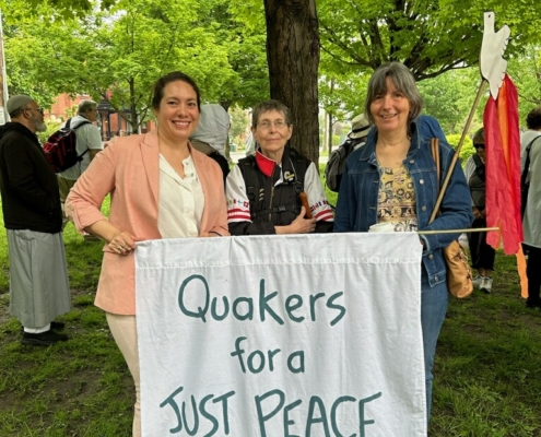 Three Quakers stand in front of a tree holding a white banner which says: Quakers for a just peace in green lettering.